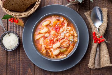 Soup with turkey, pasta, carrot, celery, tomato and cannellini beans, garnished with parmesan cheese, on the table with autumn decoration, US Thanksgiving harvest feast, horizontal, top view, closeup