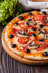 Pizza with tomato, olives, champignons, ham and cheese on round wooden plate