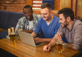 Three young men drinking beer, using lapop in pub together