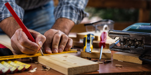 Adult carpenter craftsman with a pencil and the carpenter's square trace the cutting line on a wooden table. Construction industry, housework do it yourself. Stock photography.