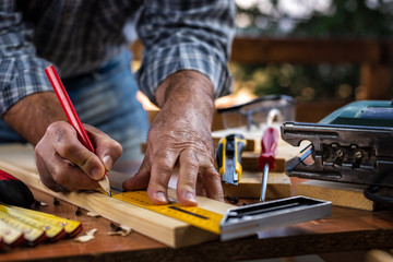 Adult carpenter craftsman with a pencil and the carpenter's square trace the cutting line on a wooden table. Construction industry, housework do it yourself. Stock photography.