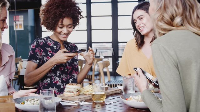 Four Female Friend Taking Pictures Of Food And Posing For Selfie In Restaurant Before Eating Meal