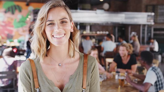 Portrait Of Waitress Holding Digital Tablet In Busy Bar Restaurant Smiling At Camera