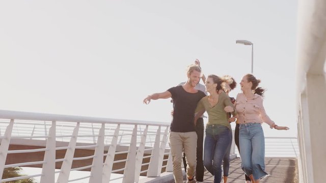 Group Of Young Friends Outdoors Walking Across Bridge Together Against Flaring Sun