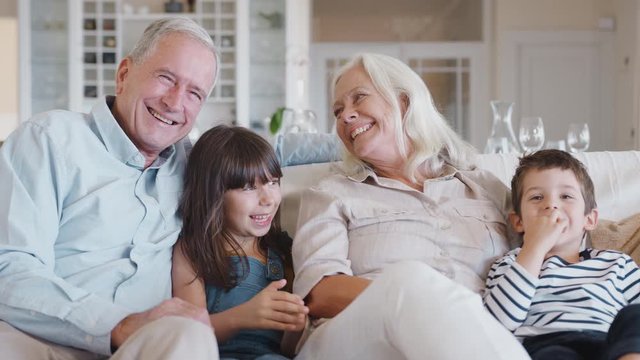 Portrait Of Smiling Grandparents Sitting With On Sofa With Grandchildren At Home