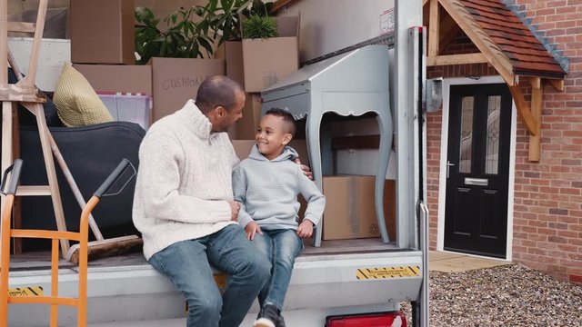 Father And Son Sitting On Tailgate Of Removal Truck On Moving Day