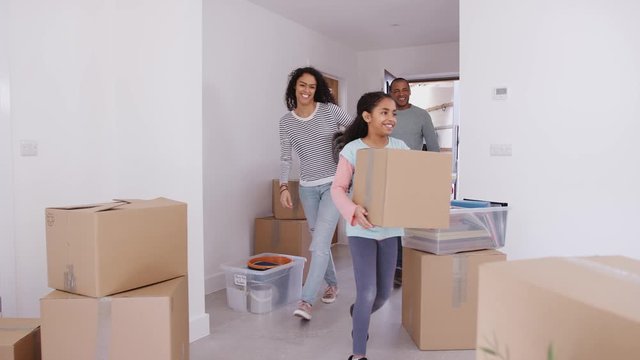 Smiling Family Carrying Boxes And Rug Into New Home On Moving Day