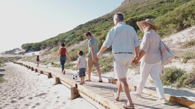 Multi-Generation Family On Summer Vacation Walking Along Wooden Boardwalk On Way To Beach