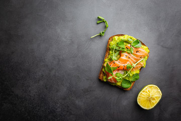 Toast with avocado cream and smoked salmon over black background, top view