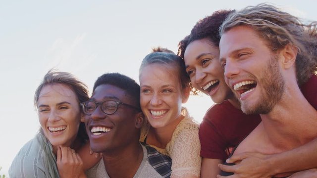 Men Giving Women Piggybacks As Group Of Friends Smile Against Flaring Sun