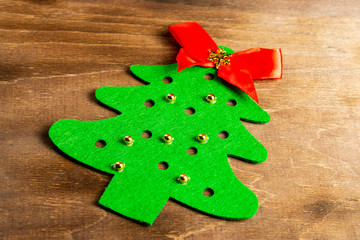 A felt christmas tree made by hands with golden bead toys and a red bow at the top lies on a wooden table. Christmas Craft