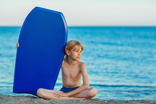 Boy with a surf board is sitting on the beach 