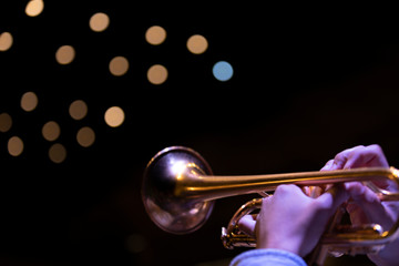 A trumpet player playing on a gold plated matte lacquered trumpet during a performance with bokeh...