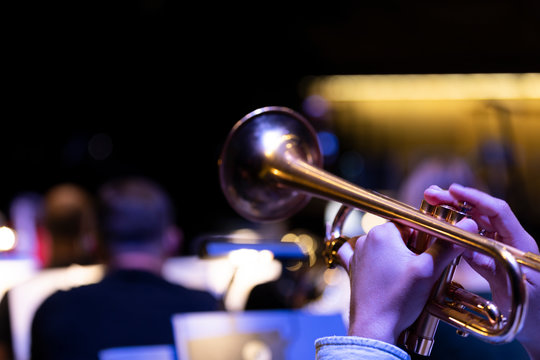 A trumpet player playing on a gold plated matte lacquered trumpet during a performance with other musicians in the background