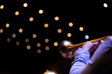 A trumpet player playing on a gold plated matte lacquered trumpet during a performance with bokeh...