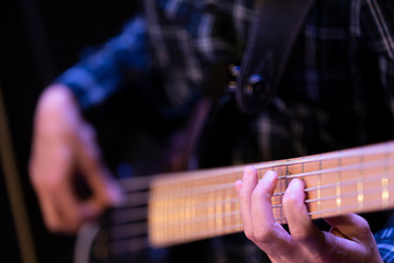 Fototapeta premium A musician dressed in a plaid, flannel shirt playing an electric bass