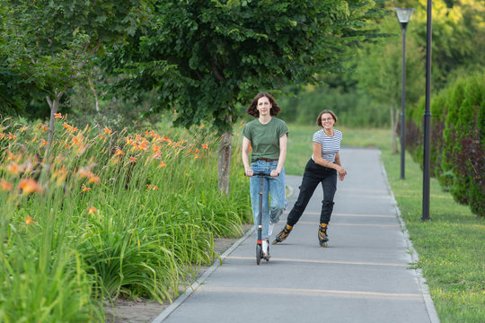Women rollerblading and riding push scooter on park footpath