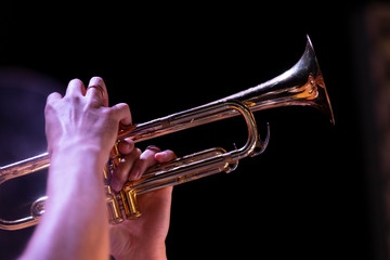 A trumpet player playing with his horn high up in a dark environment