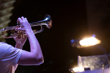 A musician playing a lacquered trumpet on stage with a music stand light shining bright next to them