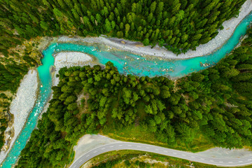 Inn River flowing in the forest in Switzerland. Aerial view from drone on a blue river in the mountains