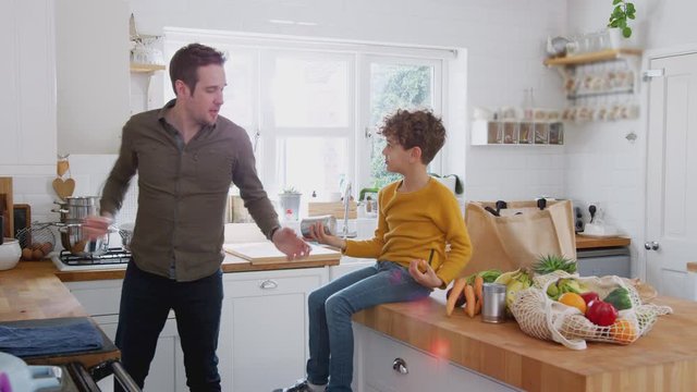 Father And Son Return Home From Shopping Trip Using Plastic Free Bags Unpacking Groceries In Kitchen