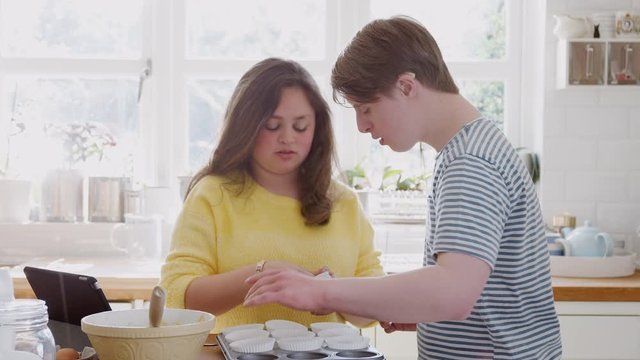 Young Downs Syndrome Couple Putting Paper Cupcake Cases Into Tray In Kitchen At Home