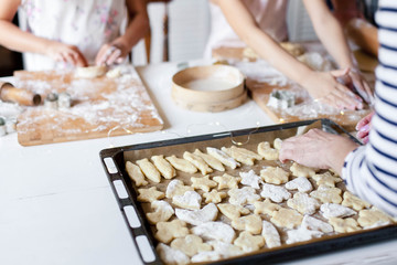 Family is cooking Christmas gingerbread cookies in home kitchen. Baking homemade pastries on oven tray. Children chef concept. Close up of hands.
