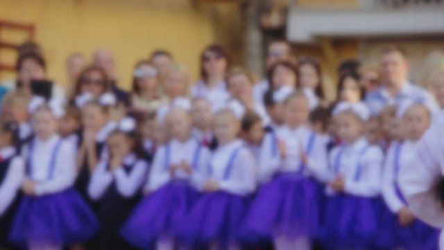 Girl in Ukrainian dress sings at the opening of the school year at school, blurred background of first graders, girls in blue dresses and white bows