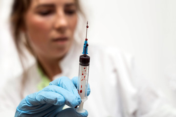 Closeup of nurse's hands with syringe of blood for cure disease, leaking blood horror scene