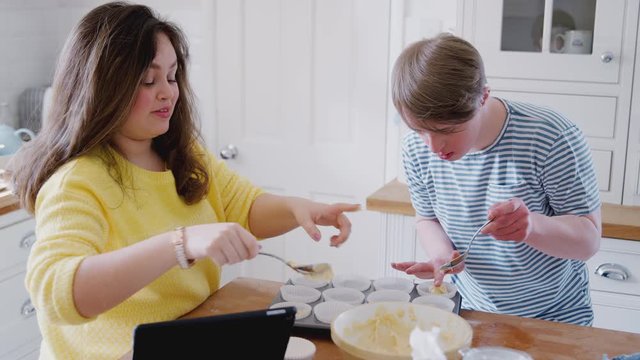 Young Downs Syndrome Couple Putting Mixture Into Paper Cake Cases In Kitchen At Home