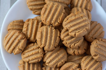 Pile of peanut butter biscuits on white plate, very tasty golden baked sweets, cookies served to eat