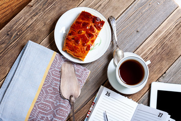 Still life with tea, cake, tablet and plan.