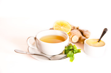 Cup of fresh ginger tea with honey, mint and cut ginger root isolated on white background. Alternative natural medicine concept. Copy space.