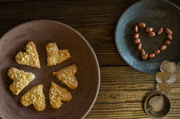 Shortbread cookies sprinkled with heart-shaped nut crumbs lie on a ceramic plate, next to peanuts laid out in the form of a heart.In the Cup is a sprig of eucalyptus with leaves like a heart. Top view