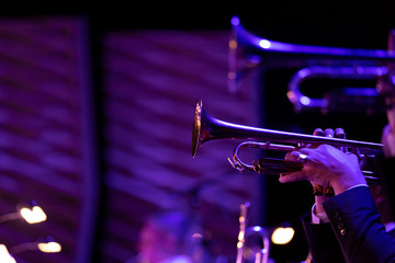 Trumpet section of a big band playing during a concert in purple stage lights