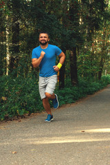 Young active handsome male healthy runner jogging outdoors along a scenic path in a forest. Vertical shot.