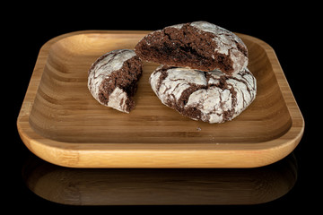 Group of one whole two halves of baked chocolate brownie cookie on wooden square plate isolated on black glass