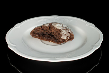 One half of baked chocolate brownie cookie on white plate isolated on black glass