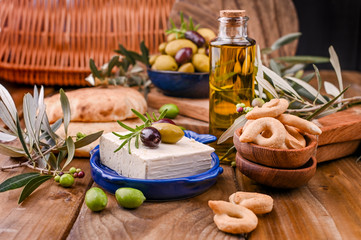 Greek cheese feta with thyme and olives, selective focus. Bread and young olives branch on olive board over old wood background. Overhead view.