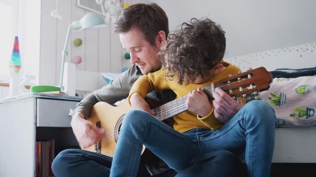 Single Father At Home With Son Teaching Him To Play Acoustic Guitar In Bedroom