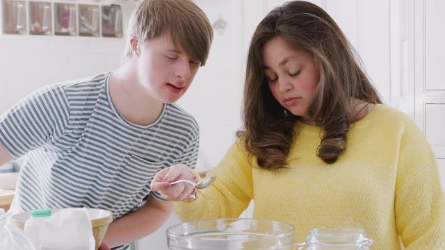 Young Downs Syndrome Couple Measuring Ingredients To Bake Cake In Kitchen At Home