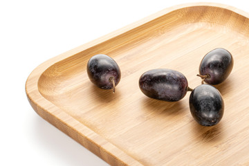 Group of four whole fresh black grape on wooden square plate isolated on white background