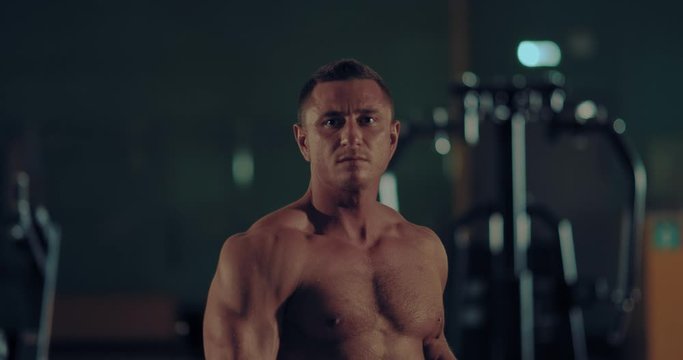 Bodybuilder shows body muscles in front of a mirror in the gym. Handsome male athlete with big chest muscles. Portrait view.