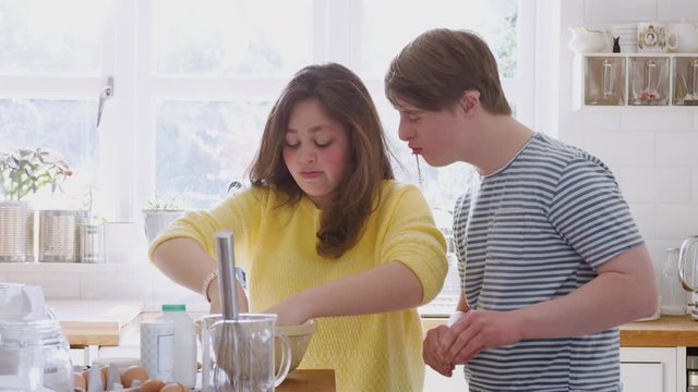 Young Downs Syndrome Couple Mixing Ingredients For Cake Recipe They Are Baking In Kitchen At Home