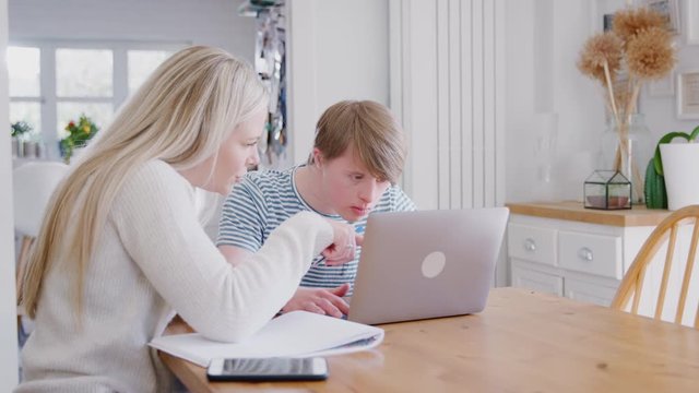 Downs Syndrome Man Sitting With Female Home Tutor Using Laptop For Lesson At Home