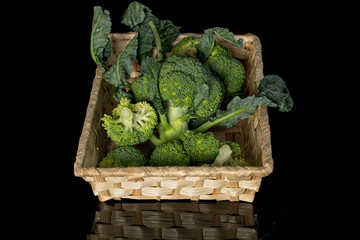 Lot of whole fresh green broccoli in braided basket isolated on black glass