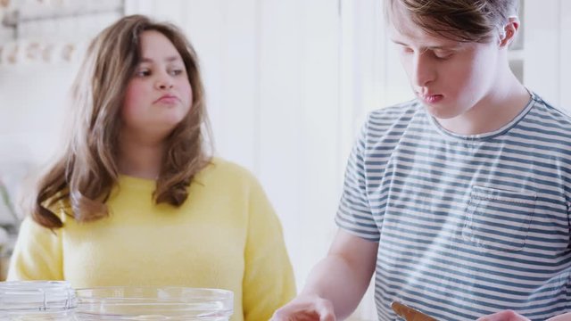 Young Downs Syndrome Couple Adding Butter To Cake Recipe They Are Baking In Kitchen At Home