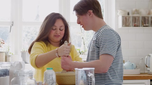 Young Downs Syndrome Couple Mixing Ingredients For Cake Recipe They Are Baking In Kitchen At Home