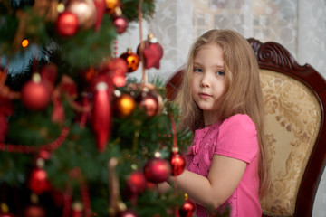Fototapeta na wymiar A little girl wearing light pink dress and looking from behind a decorated Christmas tree.