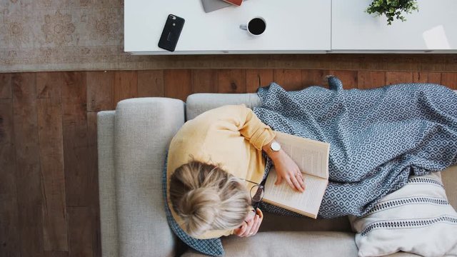 Overhead Shot Looking Down On Woman At Home Lying On Reading Book And Drinking Coffee